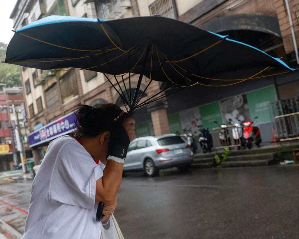 A pedestrian shields their face with an umbrella flipped by strong wind on a street in Keelung